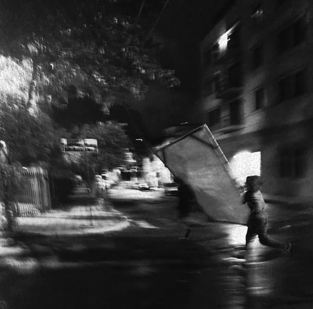 A figure carrying a canvas through a street at night